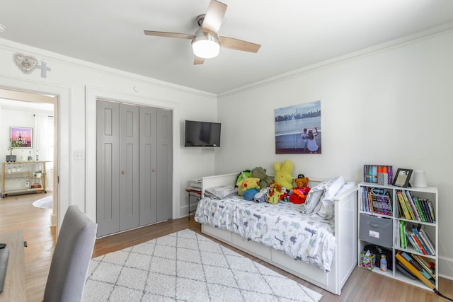 bedroom with ceiling fan, a closet, crown molding, and wood finished floors