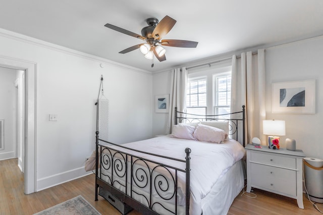 bedroom featuring a ceiling fan, crown molding, baseboards, and wood finished floors