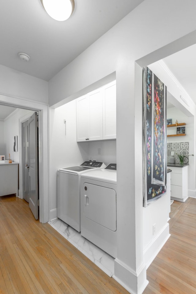 washroom featuring washing machine and dryer, cabinet space, light wood-style flooring, and baseboards