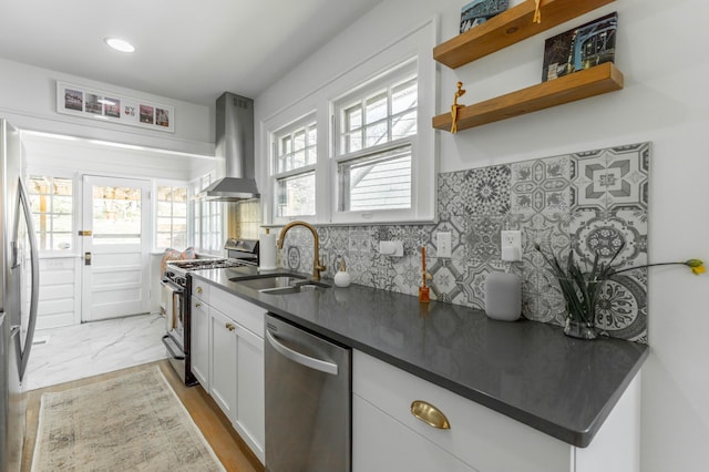 kitchen featuring stainless steel appliances, dark countertops, a sink, and wall chimney exhaust hood