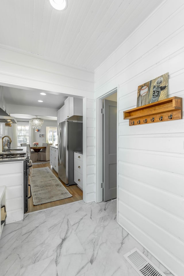 kitchen featuring visible vents, white cabinets, wall chimney exhaust hood, marble finish floor, and stainless steel appliances