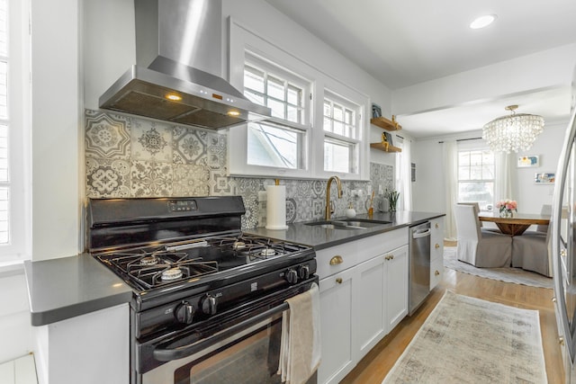 kitchen with dishwasher, dark countertops, gas range oven, wall chimney range hood, and a sink