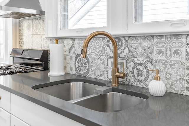 room details with a sink, white cabinetry, stainless steel gas range, decorative backsplash, and wall chimney exhaust hood