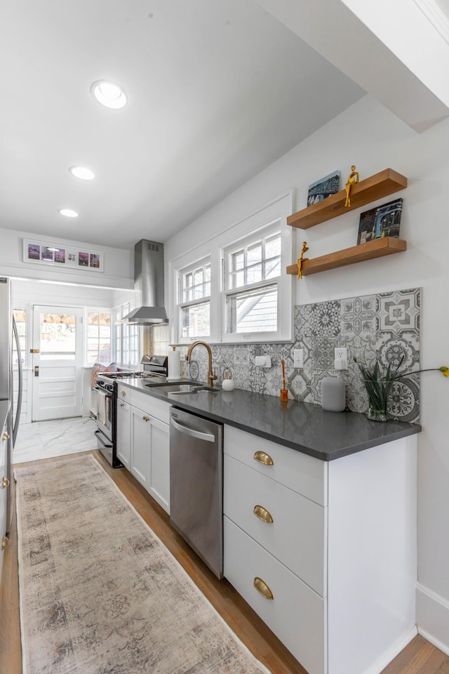 kitchen featuring tasteful backsplash, white cabinets, wall chimney exhaust hood, appliances with stainless steel finishes, and a sink