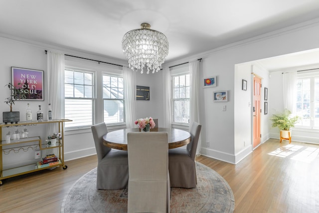 dining space with crown molding, a wealth of natural light, a notable chandelier, and light wood-style flooring