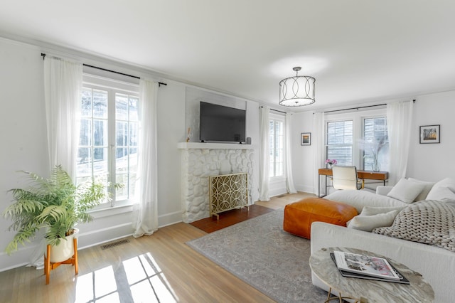 living room with visible vents, a fireplace, baseboards, and wood finished floors