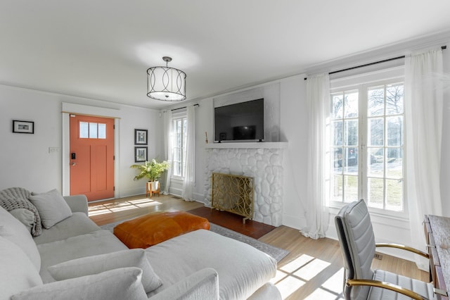 living room featuring a stone fireplace, baseboards, and wood finished floors