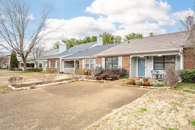 single story home featuring a porch, brick siding, and a chimney