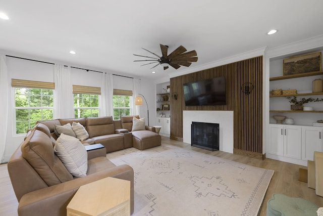 living room with light wood-type flooring, crown molding, built in shelves, and a large fireplace