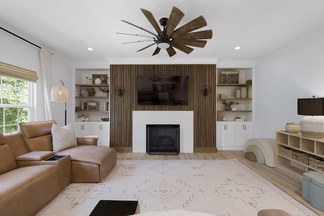 living room with light hardwood / wood-style flooring, ceiling fan, a fireplace, ornamental molding, and built in features