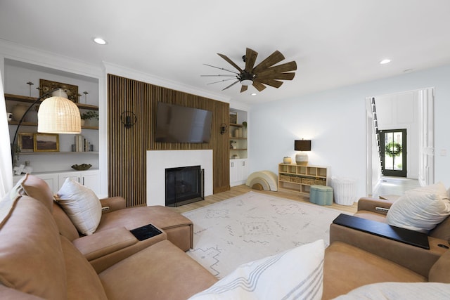 living room featuring a large fireplace, light hardwood / wood-style floors, ceiling fan, crown molding, and built in features