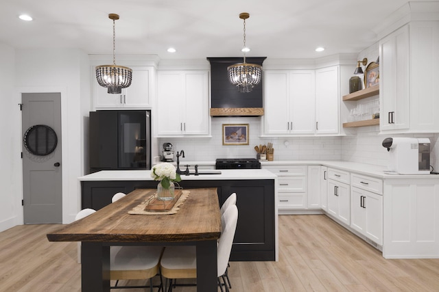 kitchen with an island with sink, fridge, white cabinetry, and pendant lighting