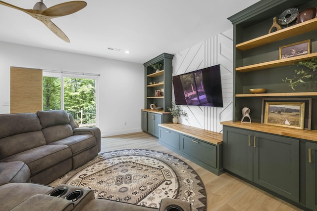 living room with light wood-type flooring, built in shelves, and ceiling fan