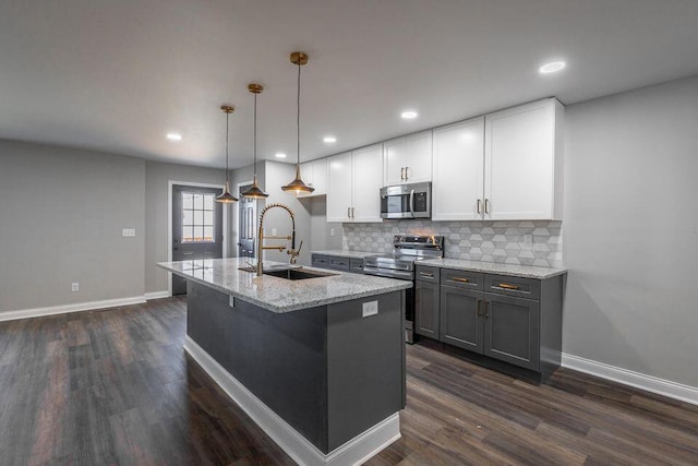 kitchen featuring light stone counters, appliances with stainless steel finishes, white cabinetry, pendant lighting, and a sink