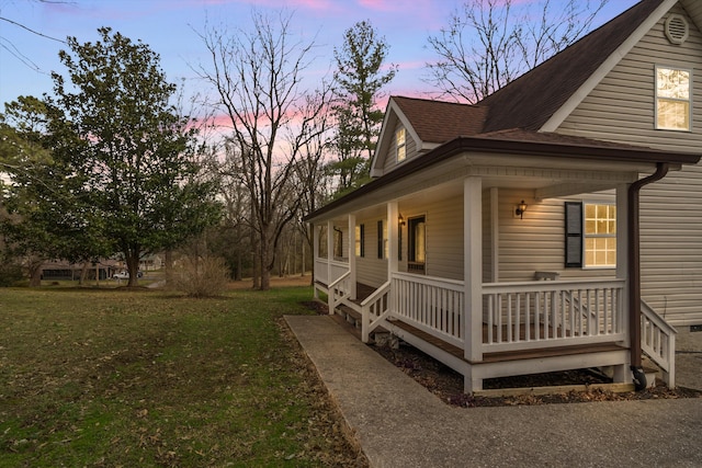 property exterior at dusk with covered porch, roof with shingles, and a lawn