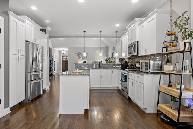 kitchen featuring stainless steel appliances, a peninsula, white cabinets, dark stone counters, and pendant lighting