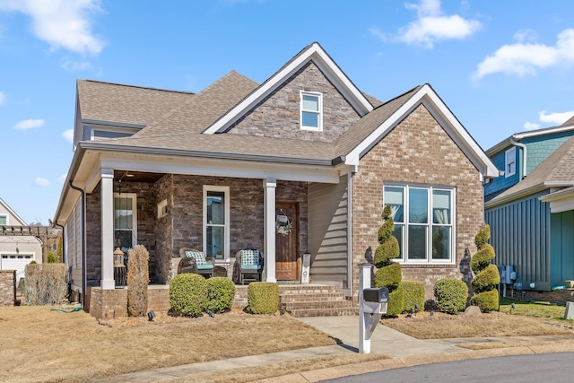 craftsman-style house featuring a shingled roof, a porch, and brick siding