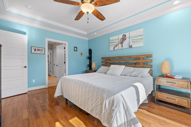 bedroom with a raised ceiling, ornamental molding, ceiling fan, wood finished floors, and baseboards