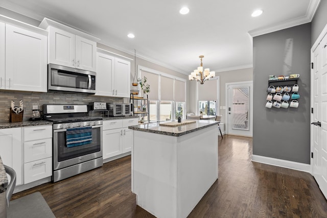 kitchen with appliances with stainless steel finishes, white cabinetry, a kitchen island, and decorative light fixtures