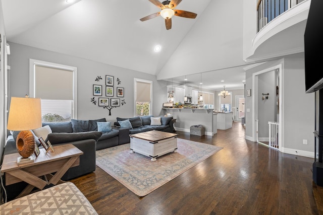 living room with baseboards, high vaulted ceiling, dark wood finished floors, and ceiling fan with notable chandelier