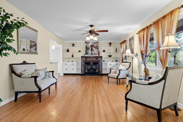 living area with baseboards, a fireplace with raised hearth, light wood-style floors, and a ceiling fan