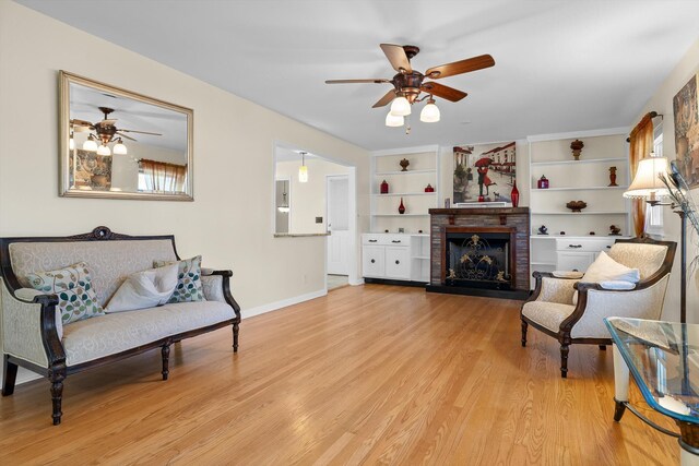 sitting room with a brick fireplace, light wood-type flooring, baseboards, and a ceiling fan