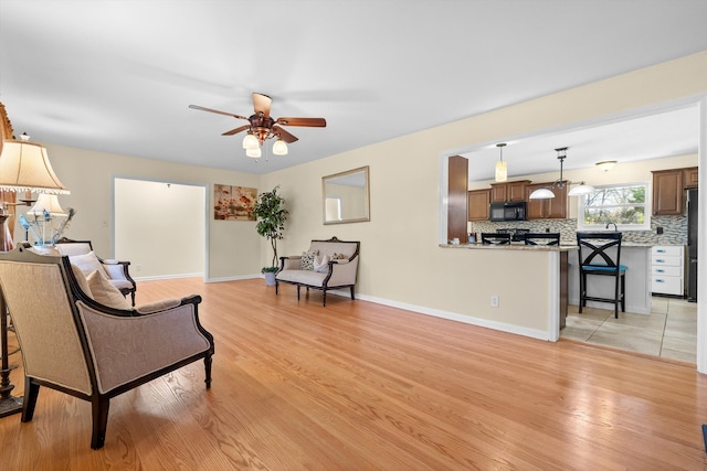 living area featuring baseboards, light wood-style floors, and a ceiling fan