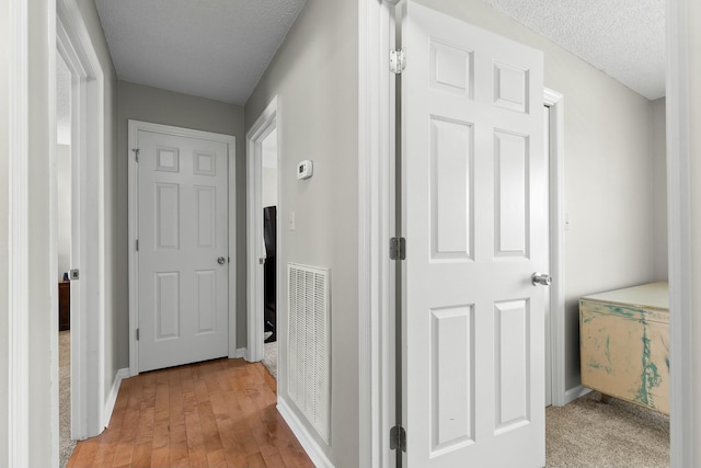 corridor with light wood finished floors, visible vents, a textured ceiling, and baseboards