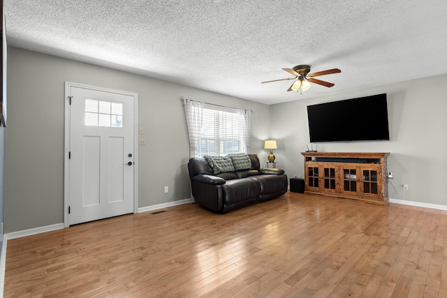 living room featuring baseboards, a textured ceiling, light wood-type flooring, and a ceiling fan