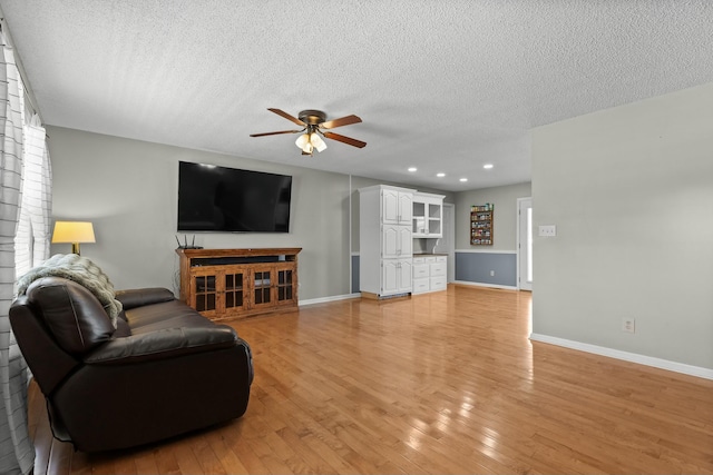 living room featuring a textured ceiling, baseboards, light wood-type flooring, and a ceiling fan