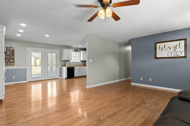 unfurnished living room featuring light wood-type flooring, baseboards, a textured ceiling, and a ceiling fan