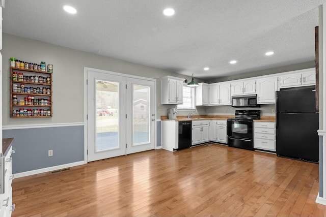 kitchen featuring white cabinetry, black appliances, light wood-type flooring, and a sink