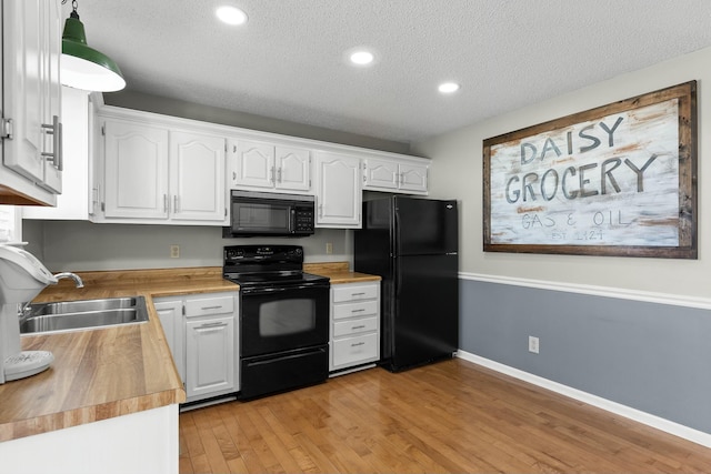 kitchen with light wood finished floors, wooden counters, a sink, black appliances, and white cabinetry