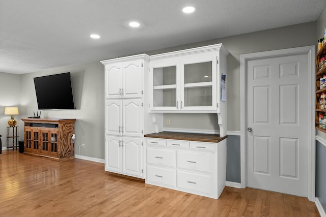 kitchen featuring light wood-type flooring, dark countertops, recessed lighting, white cabinets, and glass insert cabinets