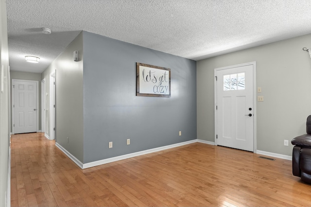 entrance foyer with light wood finished floors, visible vents, a textured ceiling, and baseboards