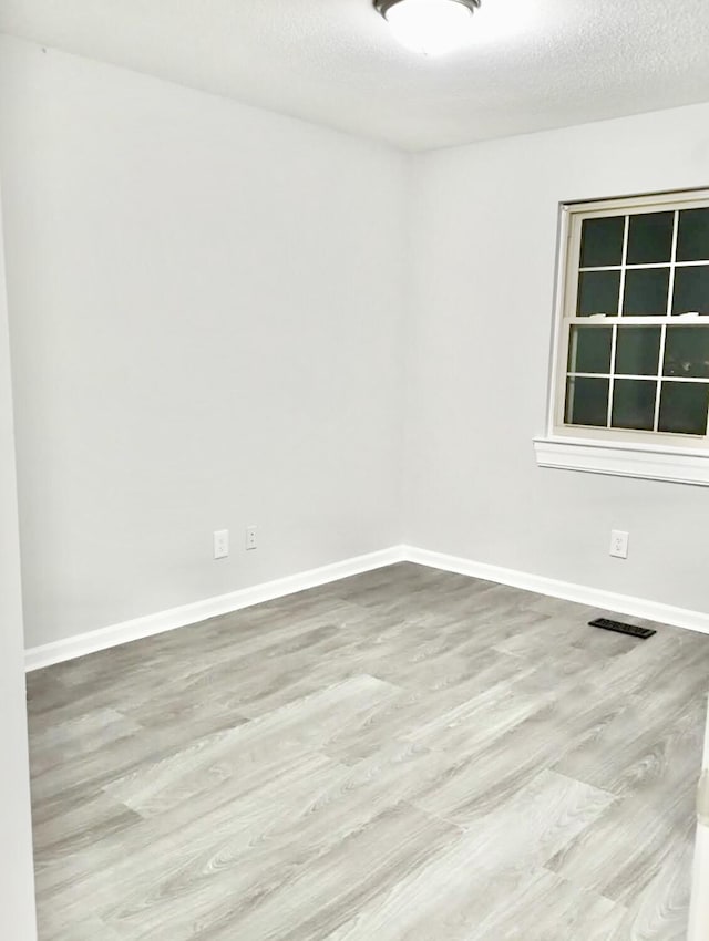 spare room with a textured ceiling and light hardwood / wood-style floors