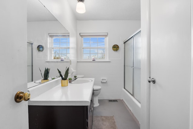 full bathroom with toilet, tile walls, combined bath / shower with glass door, concrete floors, and vanity