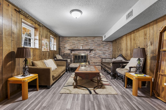 living room featuring a textured ceiling, a brick fireplace, hardwood / wood-style floors, and wood walls