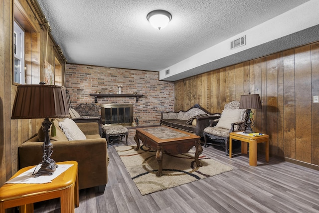 living room featuring wooden walls, a brick fireplace, a textured ceiling, and hardwood / wood-style floors