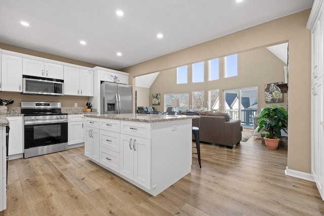 kitchen with white cabinets, light wood-type flooring, a kitchen island, and stainless steel appliances