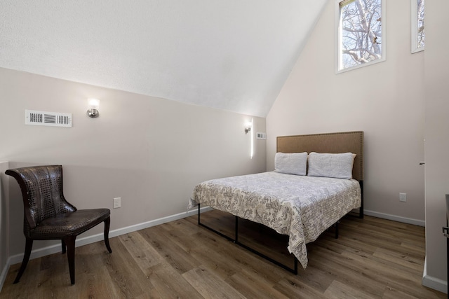 bedroom with vaulted ceiling, wood finished floors, visible vents, and baseboards