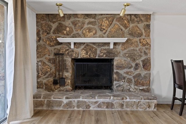 interior details with a textured ceiling, ornamental molding, wood finished floors, and a stone fireplace