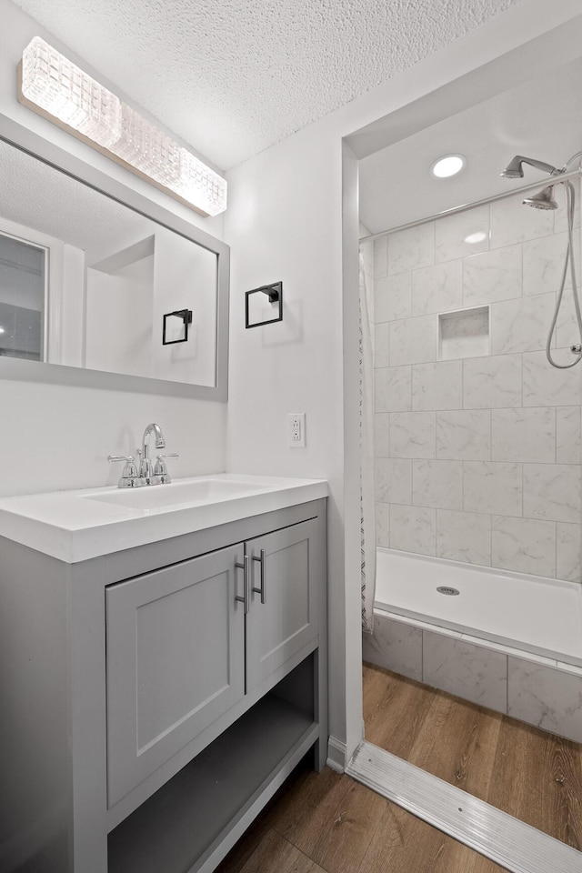 bathroom featuring a tile shower, vanity, a textured ceiling, and wood finished floors