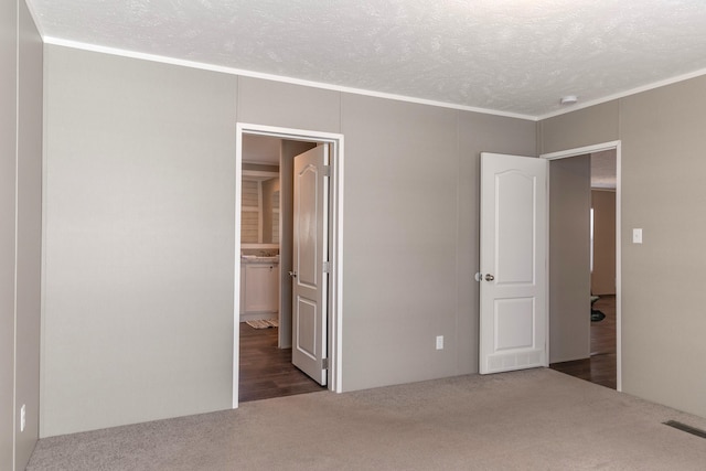 unfurnished bedroom with a textured ceiling, dark colored carpet, connected bathroom, and visible vents