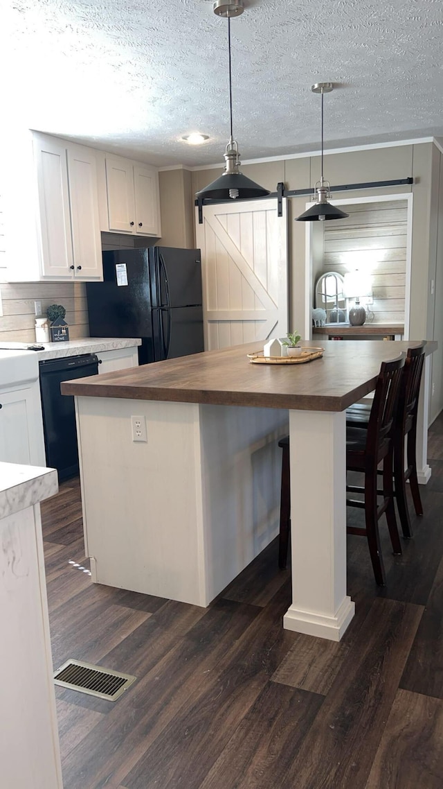 kitchen with a barn door, a kitchen island, wood counters, white cabinetry, and decorative light fixtures