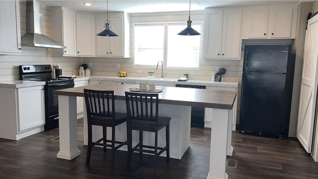 kitchen featuring wall chimney exhaust hood, white cabinetry, a kitchen island, a sink, and black appliances