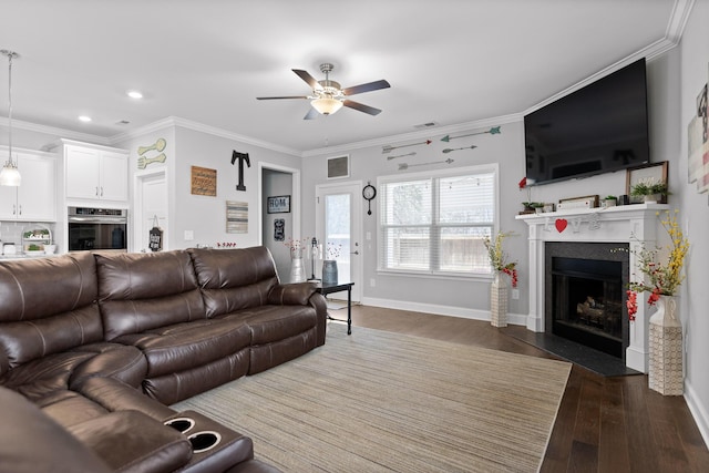 living room featuring dark wood-type flooring, a fireplace with flush hearth, a ceiling fan, visible vents, and crown molding