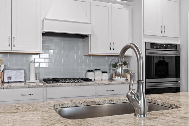 kitchen with white cabinetry, custom exhaust hood, backsplash, and a sink