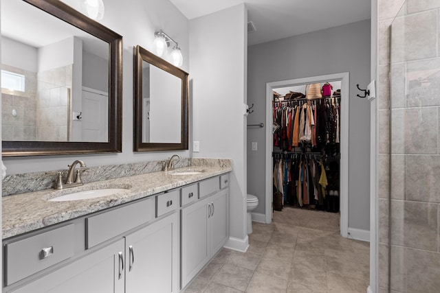 bathroom with double vanity, a walk in closet, a sink, and tile patterned floors