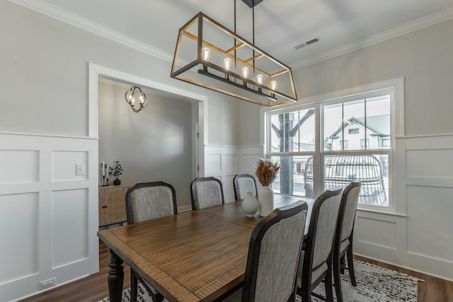 dining space featuring visible vents, ornamental molding, dark wood-type flooring, a decorative wall, and a notable chandelier